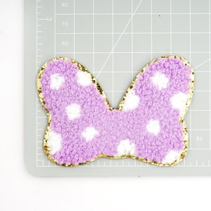 Peut inclure: Un n&oelig;ud papillon violet et blanc &agrave; pois avec une bordure dor&eacute;e paillet&eacute;e. Le n&oelig;ud est fait d'un mat&eacute;riau doux et duveteux.