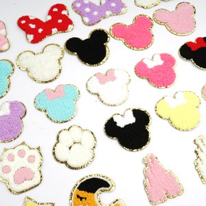 Peut inclure: Assortiment de patchs en feutre de diff&eacute;rentes couleurs avec divers motifs, notamment des oreilles de Mickey Mouse, des empreintes de pattes, des n&oelig;uds et un ch&acirc;teau. Les patchs ont une bordure dor&eacute;e paillet&eacute;e.