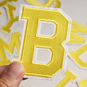May include: Yellow felt letter B with a white outline. The letter is thick and has a slightly rounded font.