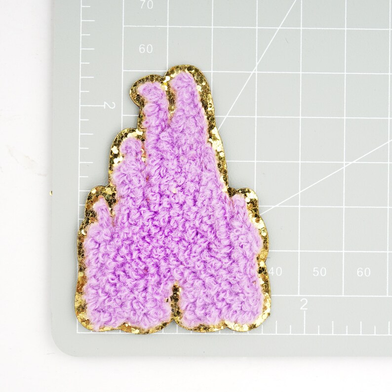 Peut inclure: Patch thermocollant en forme de ch&acirc;teau, de couleur violette et or paillet&eacute;e.