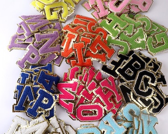 May include: Assortment of colourful felt letter patches with gold glitter trim. The letters are in various colours, including pink, blue, green, yellow, orange, purple, and black.