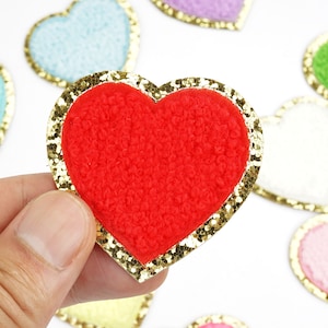 May include: A red felt heart with a gold glitter border. The heart is surrounded by other hearts in various colors and textures.