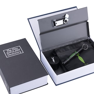 May include: A black book safe with a combination lock. The book is titled "The New English Dictionary". The safe is open and contains a small black bag, a metal grinder, and a small metal pipe.