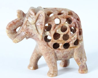 May include: A carved stone elephant figurine with a detailed design. The elephant is light brown with a reddish hue and has a hollow body with intricate cutouts.
