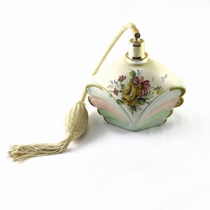 May include: A vintage perfume bottle with a floral design. The bottle is off-white with a gold-coloured top and a decorative tassel. The floral design features yellow, pink, and purple flowers. The bottle has a unique, fan-shaped base.