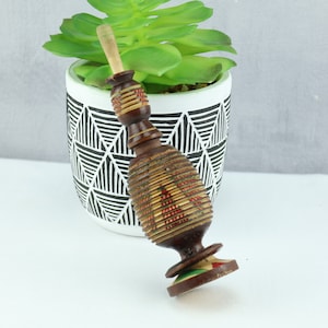 Peut inclure: Un bouchon de bouteille en bois avec un motif géométrique brun, rouge et vert. Le bouchon est en forme de bouteille et a une petite base ronde.