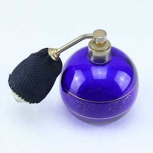 May include: A vintage cobalt blue glass atomizer bottle with a gold trim and a black fabric atomizer. The bottle has a round shape and a silver top.