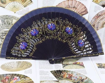 May include: A black folding fan with a blue and gold design. The fan has a carved wooden handle and is decorated with blue flowers and gold leaves.