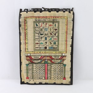 May include: A vintage-style calendar printed on papyrus paper with a black border. The calendar features the months of September and October 1994. The top of the calendar includes a chart of hieroglyphics and their corresponding letters. The calendar is decorated with a red, yellow, and blue border.