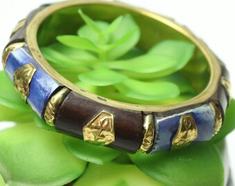 Può includere: Un braccialetto in legno con accenti blu e dorati. Il braccialetto è decorato con motivi geometrici e ha una base in legno marrone scuro.