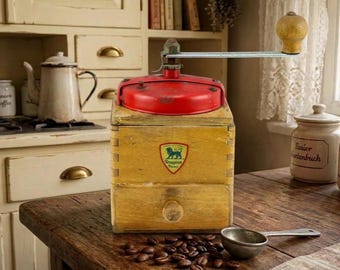 May include: A vintage wooden coffee grinder with a bright red metal top, a silver crank handle with a wooden knob, and a small drawer. A shield-shaped logo featuring a green lion and the text Peugeot Freres is centered on the front.