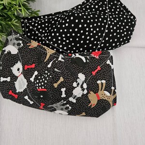 May include: Two fabric face masks. One mask is black with white polka dots. The other mask is black with a pattern of white dogs and bones.