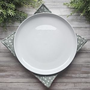 May include: A white ceramic plate with a slightly raised rim sits on a green and white polka dot fabric placemat. The placemat is folded into a triangle shape.