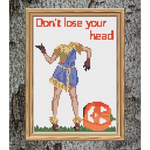 Può includere: Uno schema di ricamo a punto croce con una persona senza testa vestita di blu e giallo in piedi accanto a una zucca intagliata. Il testo "Don't lose your head" è scritto sopra la persona.