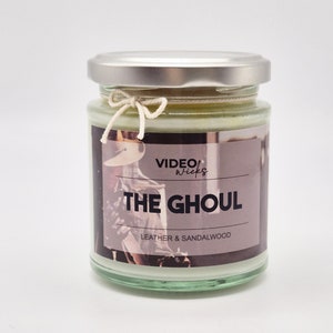 May include: A glass candle jar with a silver lid and a white string bow. The label reads "VIDEO WICKS THE GHOUL LEATHER & SANDALWOOD".