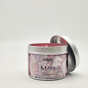 Peut inclure: Une bougie en bo&icirc;te de conserve argent&eacute;e avec un dessus de cire rouge. L'&eacute;tiquette pr&eacute;sente un design color&eacute; avec le texte "VIDEO WICKS MARKO COLA BOTTLES".