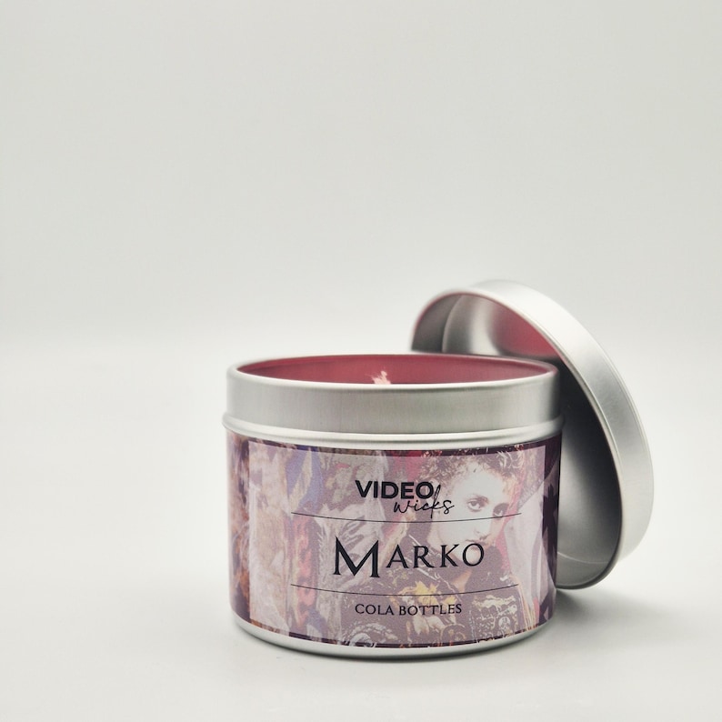 Peut inclure: Une bougie en bo&icirc;te de conserve argent&eacute;e avec un dessus de cire rouge. L'&eacute;tiquette pr&eacute;sente un design color&eacute; avec le texte "VIDEO WICKS MARKO COLA BOTTLES".