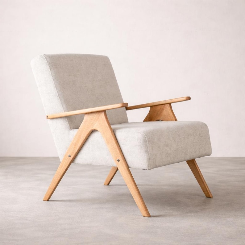May include: A mid-century modern armchair with a light gray fabric seat and back. The chair features light-colored wooden armrests and legs, with a minimalist design. The chair is set against a neutral background.