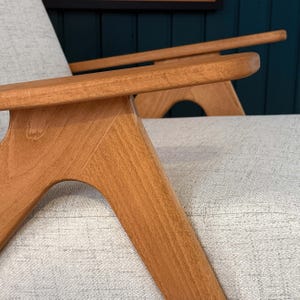 Beech armrest and sculpted leg joint with smooth grain against beige textured seat