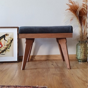 May include: A dark gray upholstered bench with a wooden frame and four legs. The bench is made of solid wood and has a simple, modern design.