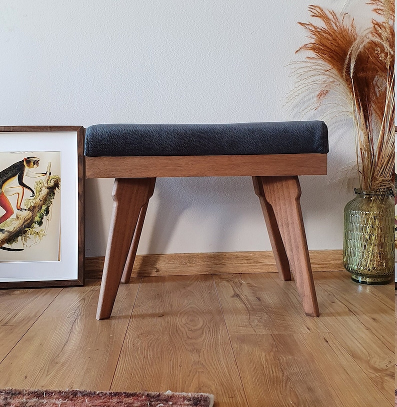 May include: A dark gray upholstered bench with a wooden frame and four legs. The bench is made of solid wood and has a simple, modern design.