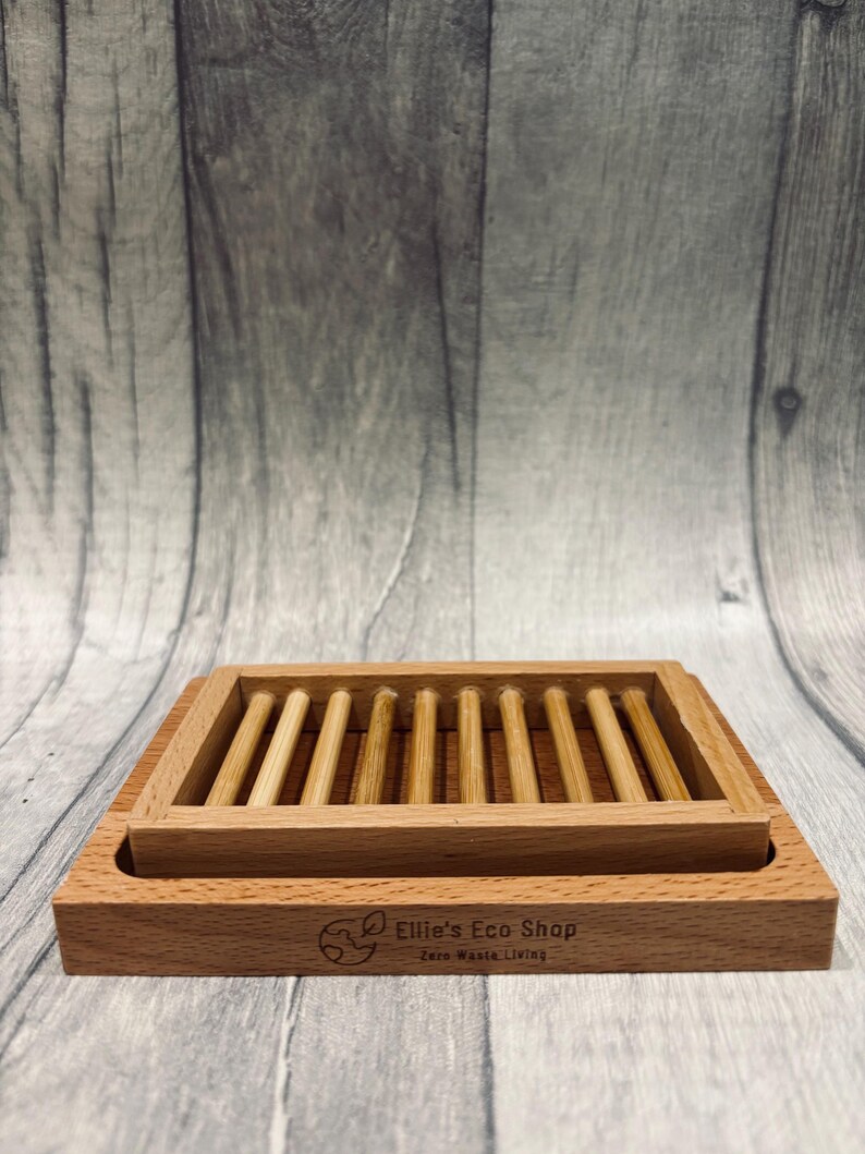 May include: A rectangular wooden soap dish with a slatted top and a lower tray. The dish is made of light brown wood and features the text "Ellie's Eco Shop Zero Waste Living".