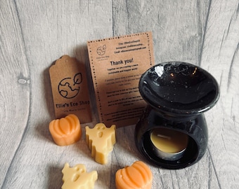 May include: A black essential oil warmer with a lit candle, accompanied by orange pumpkin and ghost-shaped wax melts. A small tag and a thank you note are also present. The text on the tag says "Ellie's Eco Shop".