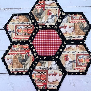 May include: A hexagonal patchwork table runner with a red and white gingham center surrounded by six hexagons featuring a rooster and chickens with a vintage farm theme.