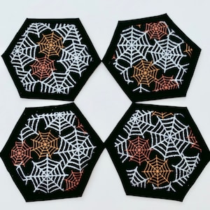 May include: Four black hexagon-shaped coasters with white and orange spiderwebs. The coasters are perfect for adding a spooky touch to your home decor.