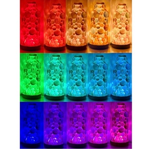 Op de afbeelding: Tien glazen lava lampen in verschillende kleuren, waaronder rood, oranje, geel, groen, blauw, paars en roze. Elke lamp heeft een ronde basis en een transparante glazen cilinder gevuld met gekleurde was.