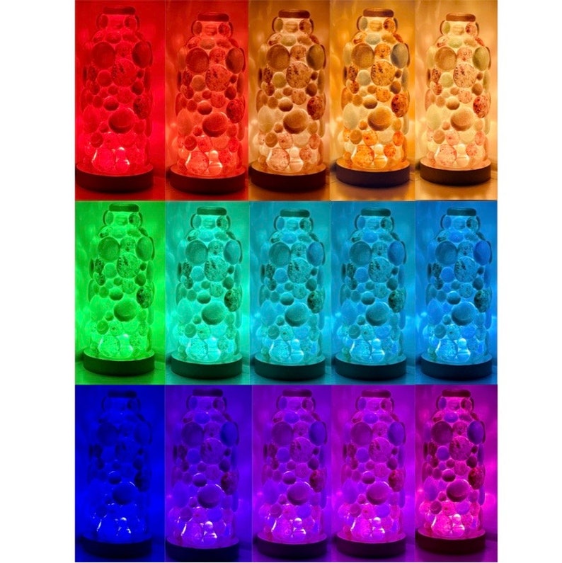 Op de afbeelding: Tien glazen lava lampen in verschillende kleuren, waaronder rood, oranje, geel, groen, blauw, paars en roze. Elke lamp heeft een ronde basis en een transparante glazen cilinder gevuld met gekleurde was.