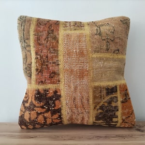 May include: A patchwork cushion with a brown, orange and beige colour scheme. The cushion is made of woven fabric with a variety of patterns.