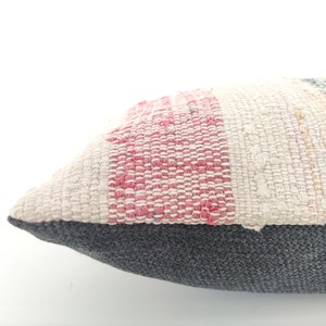 May include: A rectangular pillow with a striped pattern in shades of pink, white, and green. The pillow has a gray fabric backing.