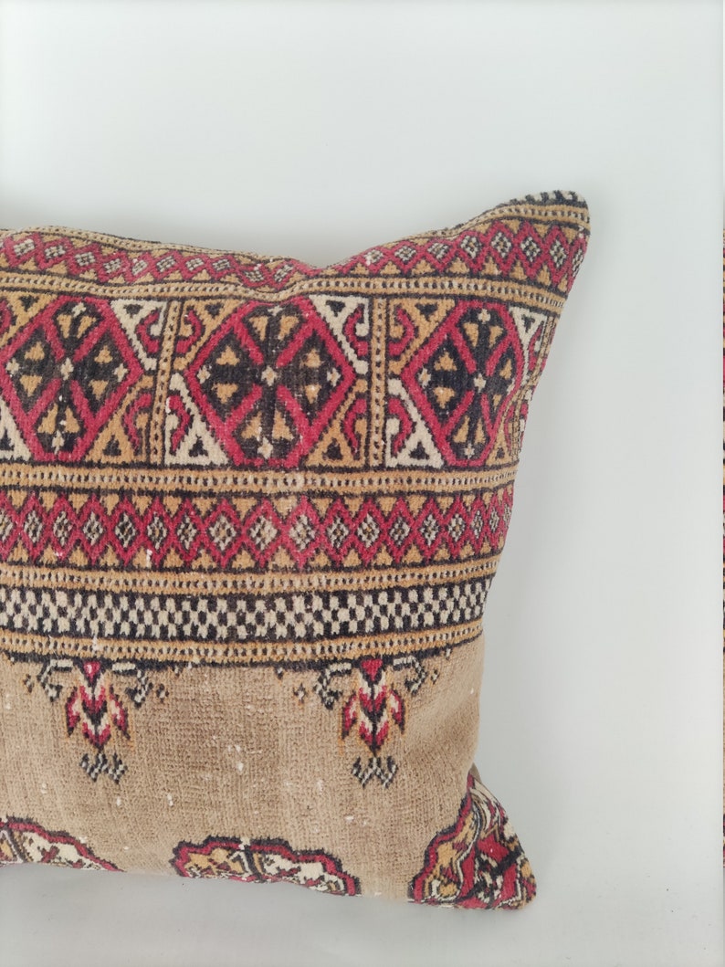 May include: A rectangular pillow with a brown background and a colorful geometric pattern in red, black, and yellow. The pillow is made of a soft, woven fabric.