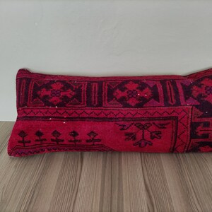 May include: A red and black patterned lumbar pillow with a traditional design. The pillow is made of woven fabric and has a rectangular shape.