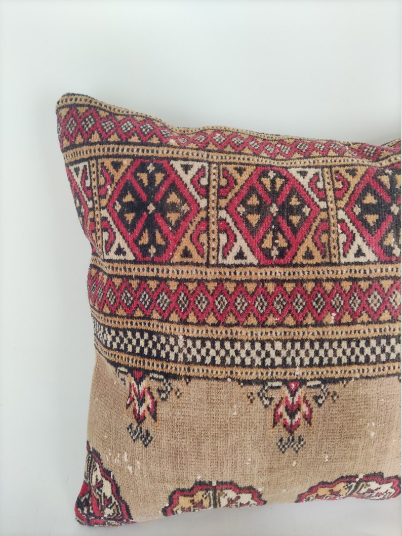 May include: A rectangular pillow with a brown, red, and black geometric pattern. The pillow has a fringe border and is made of a soft, woven fabric.