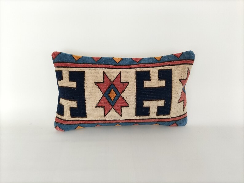 May include: A rectangular throw pillow with a geometric pattern in shades of blue, red, orange, and white. The pillow has a cream-colored background and a blue border.