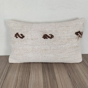 May include: A white rectangular pillow with brown embroidered designs. The pillow is made of a soft, textured fabric.
