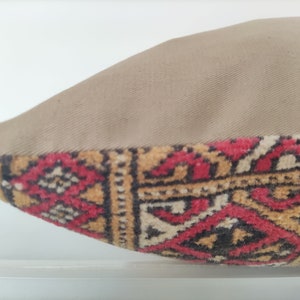 May include: A beige pillow with a red, black, and gold patterned fabric on the bottom edge.