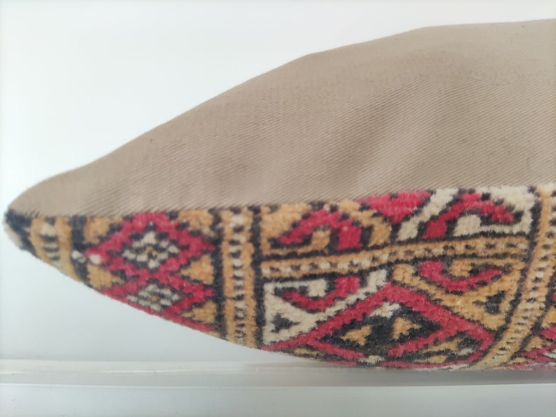 May include: A beige pillow with a red, black, and gold patterned fabric on the bottom edge.