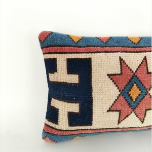 May include: A long, rectangular pillow with a cream-colored background and a colorful geometric pattern. The pattern features blue, pink, and yellow colors in a repeating design.