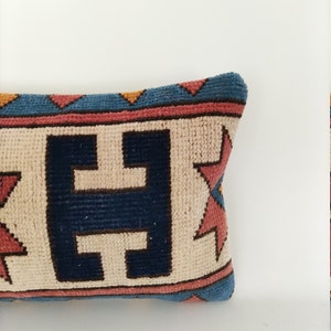 May include: A decorative pillow with a geometric pattern in shades of blue, red, and yellow. The pillow has a cream-colored background with a dark blue pattern in the center.
