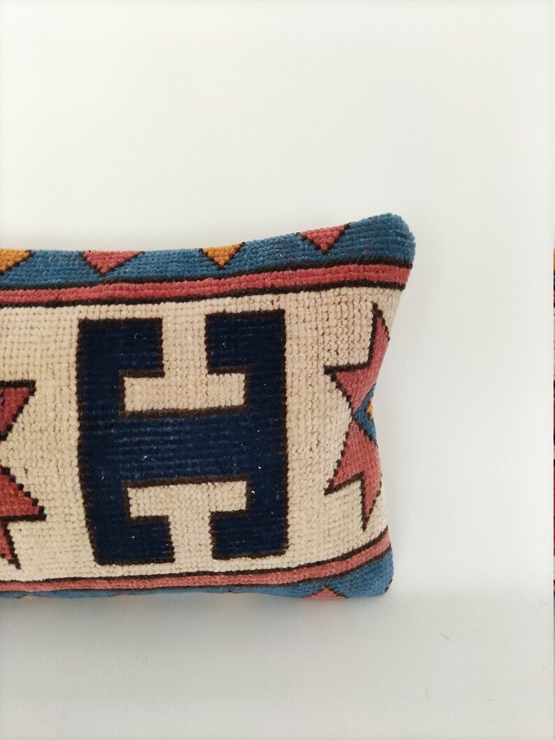 May include: A decorative pillow with a geometric pattern in shades of blue, red, and yellow. The pillow has a cream-colored background with a dark blue pattern in the center.