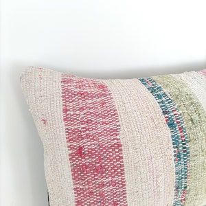May include: A white pillow with pink, green, and blue stripes. The pillow is made of a woven fabric and has a slightly distressed look.
