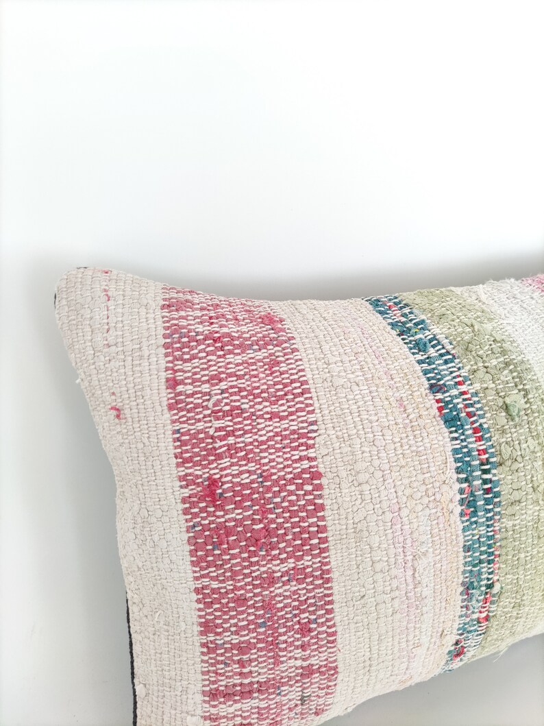 May include: A white pillow with pink, green, and blue stripes. The pillow is made of a woven fabric and has a slightly distressed look.