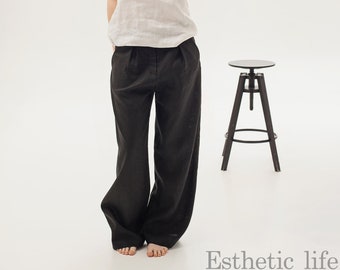 May include: A woman wearing a white linen tank top and black wide-leg linen pants. She is standing in front of a black metal stool. The text "Esthetic life" is written in white at the bottom of the image.