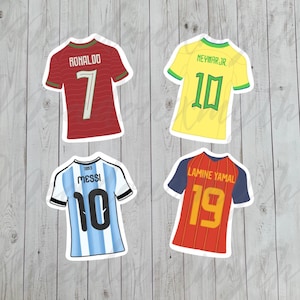 Puede incluir: Cuatro pegatinas de camisetas de fútbol con nombres y números: una roja de Ronaldo 7, una amarilla de Neymar Jr. 10, una de rayas azul claro y blanco de Messi 10 y una roja y azul de Lamine Yamal 19. Cada pegatina tiene un borde blanco.