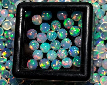 May include: A close-up of a small black box filled with iridescent opal gemstones. The box is surrounded by a large quantity of loose opal gemstones.