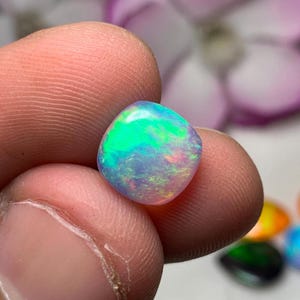 May include: A vibrant, iridescent opal gemstone with a square shape. The opal displays a range of colors, including green, blue, pink, and yellow.