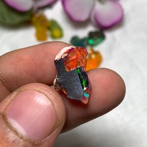 May include: A small, rough, orange, green and black opal gemstone with iridescent flashes.